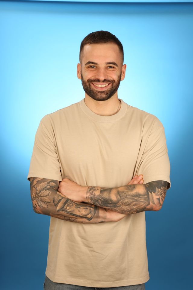 Alessandro Guidoni sorridente a braccia incrociate su fondo azzurro